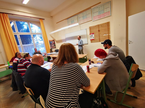 tantermi kép, felnőtt tanulók ülnek a padokban, hallgatják a férfi tanárt, akik filces tábla előtt magyaráz