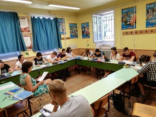 tantermi fotó körbe tett padokkal, középen tanár felolvas