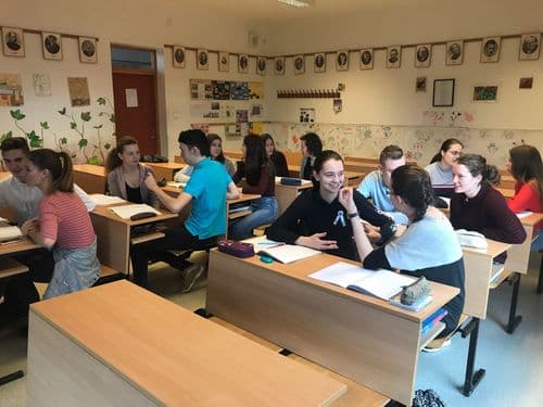 tantermi kép, tanulók ülnek a padokban, vidáman beszélgetnek, a tanár sehol. Az előtérben az első pad üres.