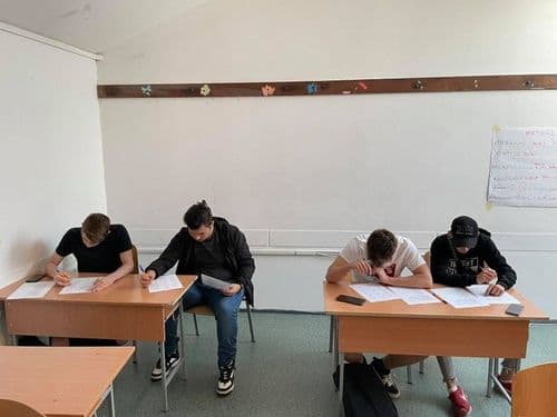 Tanulók csoportja a Lépj feljebb-projekt keretében. Négyen ülnek két padban, mindegyikük papírokat tölt ki tollal a kezében, az egyiken még baseball-sapka is van, de legalább nem fordítva.