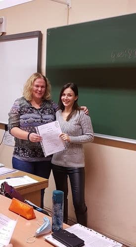 Tábla előtt áll egy tanárnő egy lánytanulóval együtt, és büszkén tartanak egy vszc logós oklevelet