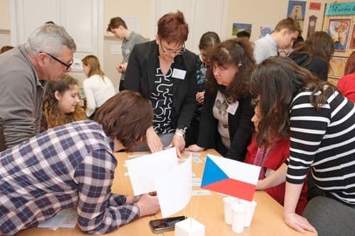 Cseh nap, a tanárok asztala, körülállják az asztalt és papírcetliket rendeznek, cseh zászló az asztalon