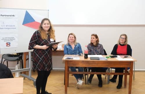 Cseh nap, eredményhirdetés. A három tagú zsűri az asztalnál ül, az egyik szervező előttük áll és felolvassa a nyertes csapatok nevét