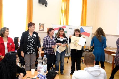 Cseh nap, a tanáros az eredményhirdetésnél a tábla előtt állnak, mutatják a Váci SZC Országnapok logós vászonszatyrot, amit nyertek