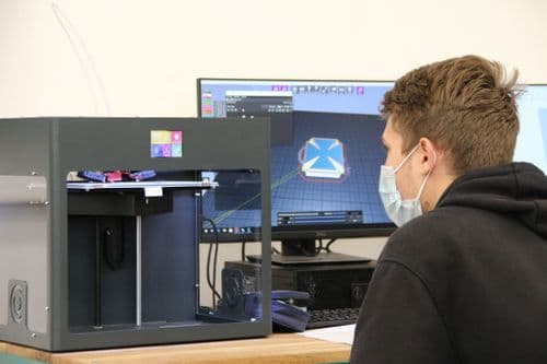 Tanuló 3D nyomtatóval nyomtat egy asztalnál ülve a DKA tanteremben
